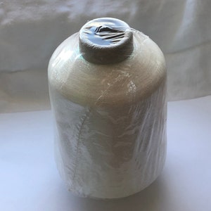 Puede incluir: Una bobina de hilo blanco envuelta en plástico transparente. La bobina está envuelta en una envoltura de plástico transparente.
