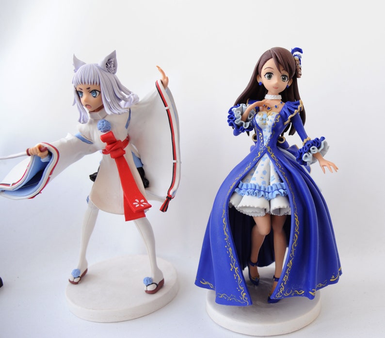 K&ouml;nnte beinhalten: Zwei Anime-Figuren. Eine ist eine wei&szlig; gekleidete Figur mit Fuchsohren und einem roten Band. Die andere ist eine Frau in einem blau-wei&szlig;en Kleid mit goldenen Akzenten. Beide Figuren stehen auf wei&szlig;en, kreisf&ouml;rmigen Sockeln.