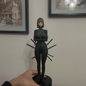 May include: A black figurine of a woman in a form-fitting outfit, with multiple swords attached. The figure has short brown hair and is standing on a black circular base. The swords have black blades and green handles.