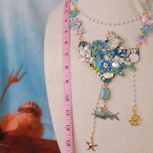 May include: A multi-strand necklace with a large, colorful pendant featuring seashells, starfish, and a fish. The pendant is made of various materials, including beads, metal, and resin. The necklace is approximately 18 inches long.
