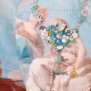 May include: A blue and green statement necklace with a seashell and starfish design. The necklace features a variety of beads, including pearls, turquoise, and gold.