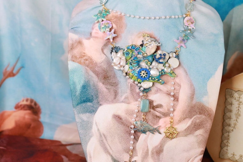 May include: A blue and green statement necklace with a seashell and starfish design. The necklace features a variety of beads, including pearls, turquoise, and gold.