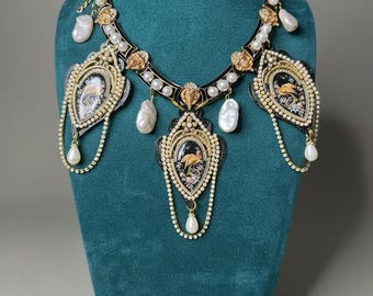 May include: An ornate necklace with black, gold, and pearl accents. The necklace features three pendant-like elements with miniature paintings and dangling pearl drops. The necklace is displayed on a teal mannequin.