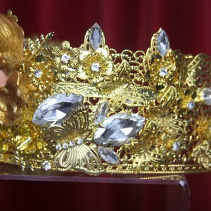 May include: A gold crown with clear crystal accents and a cherub figure on the side.