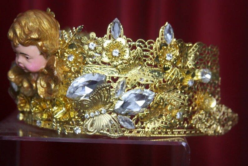 May include: A gold crown with clear crystal accents and a cherub figure on the side.