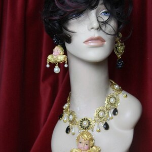May include: A gold crown with clear and yellow rhinestones, a gold necklace with black and white beads and a cherub pendant, and matching earrings with cherub pendants.