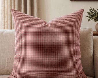 May include: A square throw pillow featuring a classic red and white gingham check pattern. The fabric displays a consistent, small-scale checkered design across the entire surface, creating a uniform grid appearance on this decorative cushion.