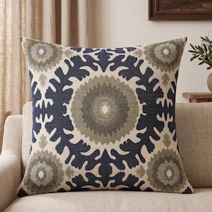 May include: A square throw pillow featuring a cream-colored base with a large, centered circular medallion pattern in navy blue and olive green. The design includes intricate, symmetrical floral-inspired shapes and repeating circular motifs.