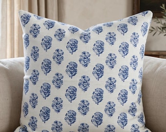 May include: A square throw pillow featuring a repeating pattern of blue floral motifs printed on an off-white fabric base. The design consists of small, stylized flower clusters arranged in vertical columns across the entire surface of the pillow.