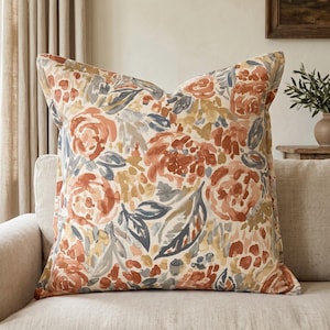 May include: A square throw cushion featuring a watercolour-style floral pattern in shades of terracotta, muted blue, and soft yellow on a cream background. The design displays abstract painted flowers and foliage across the entire fabric surface.