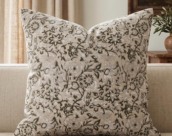 Könnte beinhalten: Ein quadratisches Zierkissen mit beigem Stoffgrund und einem dunkel olivgrünen Blumenmuster. Das Design besteht aus komplexen, sich wiederholenden botanischen Motiven, darunter stilisierte Blüten, Blätter und sich windende Ranken auf der gesamten Oberfläche.