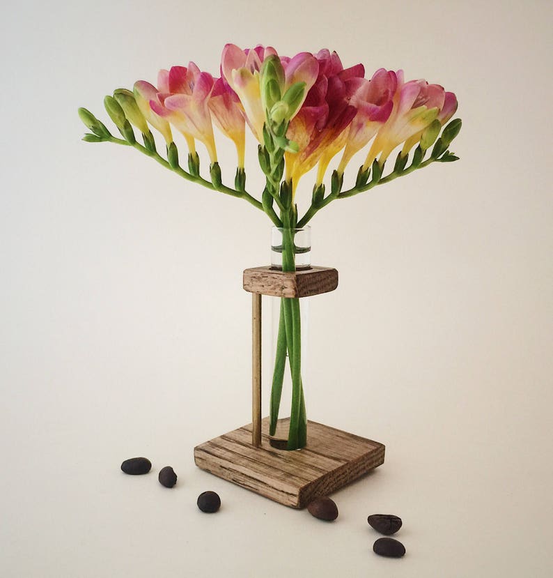 May include: A wooden flower vase with a glass test tube insert. The vase is made of rustic wood and has a square base. The test tube is filled with pink and yellow freesia flowers.