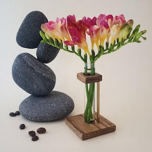 May include: A wooden flower vase with a glass tube for holding flowers. The vase is sitting on a table with a stack of gray stones and coffee beans.