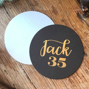 May include: A black round coaster with the name "Jack" and the number "35" written in gold lettering.