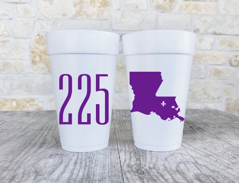 May include: Two white foam cups. The left cup features the purple text 225. The right cup displays a purple silhouette of the state of Louisiana with a small purple fleur-de-lis symbol positioned within the state outline on the cup surface.
