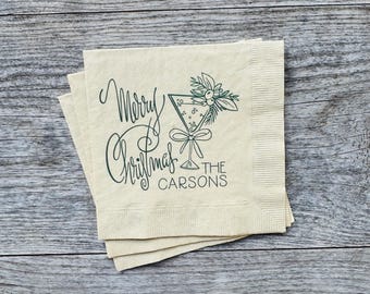 May include: A stack of beige paper napkins with a green holiday design. The napkins feature the words "Merry Christmas" in elegant script, along with a martini glass illustration and the name "The Carsons".