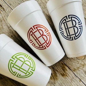 May include: Three white foam cups with a monogram design in red, blue, and green. Each cup features a circular design with the intertwined letters "EB". The cups are arranged on a rustic wooden surface.