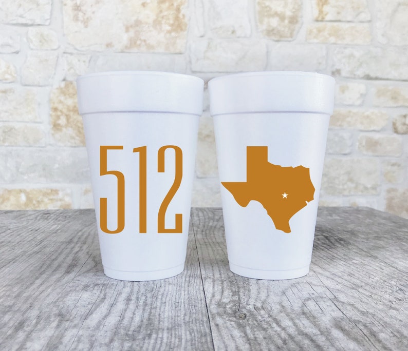 May include: Two white foam cups. One cup features the orange numbers 512 printed on the front. The other cup displays an orange silhouette of the state of Texas with a small white star marking a location within the state boundaries.
