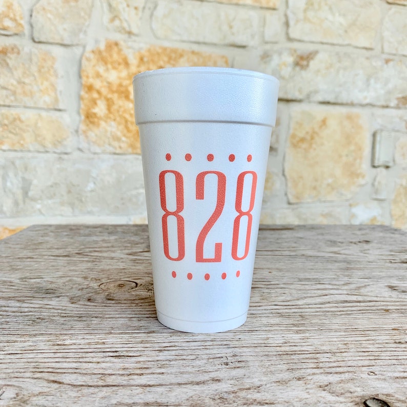 May include: A white foam cup featuring the number 828 printed in a coral-colored sans-serif font on the front. The number is centered between two horizontal rows of five small coral-colored dots, with one row above and one row below the text.