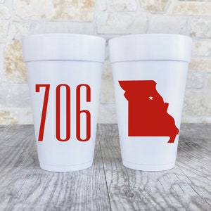 May include: Two white foam cups. The left cup features the red numbers 706 in a tall, sans-serif font. The right cup displays a solid red silhouette of the state of Missouri with a small white star marking a specific location within the state borders.