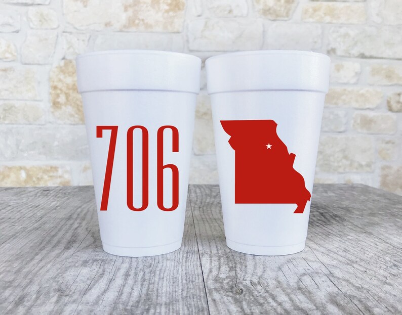 May include: Two white foam cups. The left cup features the red numbers 706 in a tall, sans-serif font. The right cup displays a solid red silhouette of the state of Missouri with a small white star marking a specific location within the state borders.