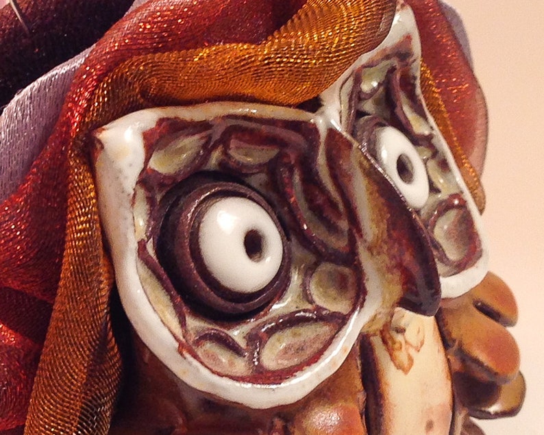 May include: Close-up of a ceramic owl sculpture with white eyes and brown details. The owl is decorated with a red and orange fabric.