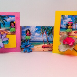 May include: Three handmade greeting cards with tropical beach scenes and hula girl figurines. Each card features a different colored background, a flower embellishment, and a tropical scene with palm trees and a beach.