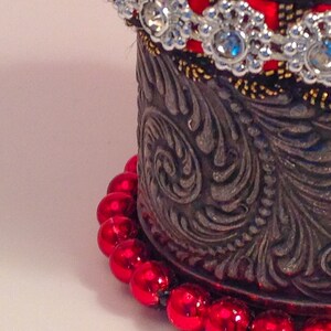 May include: A silver metal container with an ornate design and a red beaded trim. The container has a red and silver beaded trim.