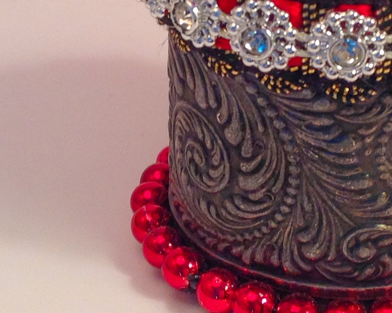May include: A silver metal container with an ornate design and a red beaded trim. The container has a red and silver beaded trim.