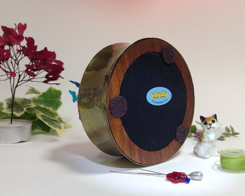 May include: A brass and wood base with a felt bottom and a sticker that reads "Wonderland in Jars". The base is decorated with colorful butterflies.