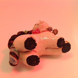 May include: A white ceramic figurine of a pig wearing a red and gold hat and a blue and gold scarf. The pig has black hooves and is lying on its side.