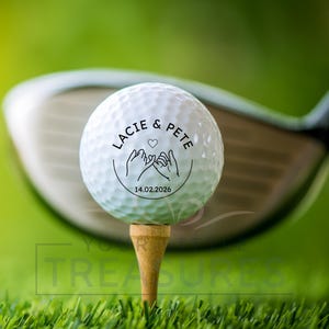 May include: A white golf ball on a wooden tee, with a golf club in the background. The ball is printed with the names "Lacie & Pete", a heart, clasped hands, and the date 14.02.2026. The scene is set on a green golf course.