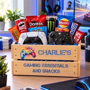 May include: A wooden crate filled with snacks and two game controllers. The crate features a colourful controller graphic and the text "CHARLIE'S GAMING ESSENTIALS AND SNACKS". Inside are Pringles, Doritos, M&Ms, Monster energy, Walkers, Snickers, and KitKat.