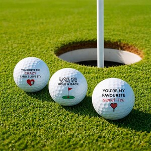 May include: Three white golf balls with text and heart graphics on a green golf course. The text on the balls reads: "YOU DRIVE ME CRAZY (AND I LOVE IT)", "I LOVE YOU TO THE 9TH HOLE & BACK", and "YOU'RE MY FAVOURITE sweet-tee".