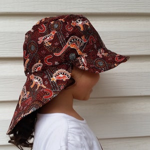 Peut inclure: Un chapeau de soleil rouge et brun avec un motif aborigène australien représentant des kangourous et d'autres animaux. Le chapeau a une large bordure et un rabat qui peut être rabattu pour protéger le cou.