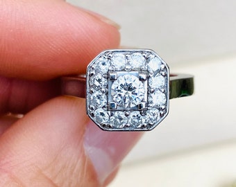 Könnte beinhalten: Ein silberner Ring mit einem großen, runden, klaren Diamanten, der von kleineren Diamanten in einer quadratischen Fassung umgeben ist.