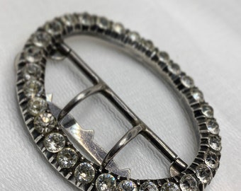 May include: A silver oval buckle with a row of clear rhinestones around the edge.
