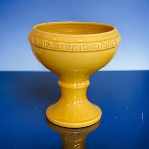 May include: A yellow ceramic pedestal bowl with a geometric design around the rim.