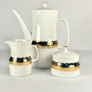 May include: A white porcelain coffee pot, creamer, and sugar bowl set with a gold and black trim. The set features a decorative design with gold accents.