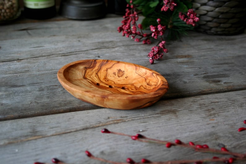 May include: A natural wood soap dish with a light brown color and a smooth, oval shape. The dish has three small holes in the bottom for drainage.
