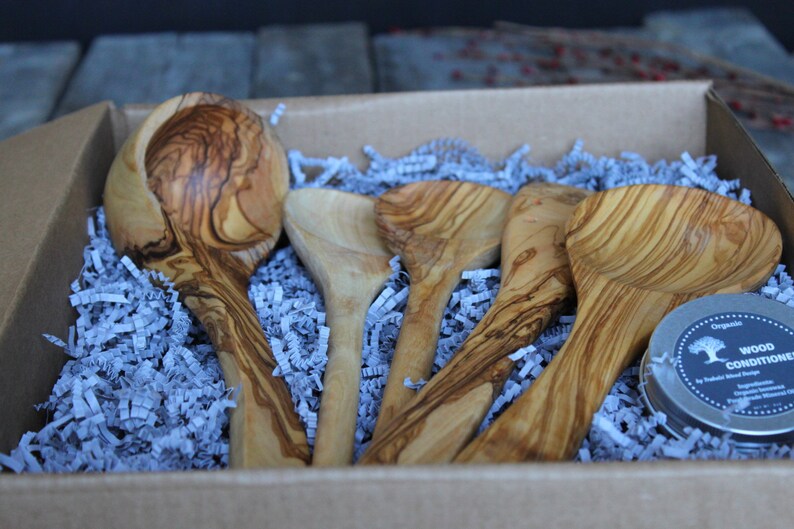 Puede incluir: Un juego de cinco utensilios de cocina de madera de olivo en una caja de cart&oacute;n con papel de seda azul. El juego incluye un cuchar&oacute;n grande, dos cucharones m&aacute;s peque&ntilde;os y dos cucharas. Tambi&eacute;n se incluye un peque&ntilde;o bote de acondicionador para madera.