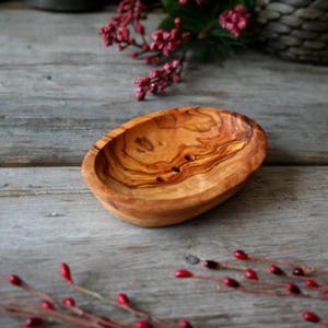 May include: A natural wood soap dish with a light brown color and a smooth, oval shape. The dish has two small holes in the bottom for drainage.
