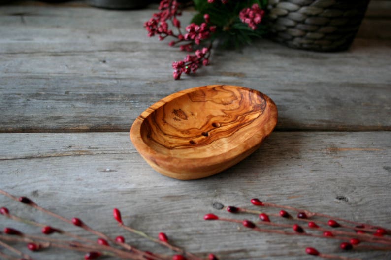 May include: A natural wood soap dish with a light brown color and a smooth, oval shape. The dish has two small holes in the bottom for drainage.