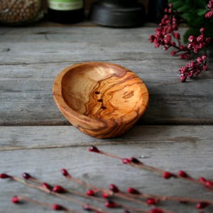 May include: A natural wood soap dish with a light brown color and a grain pattern. The dish has three small holes in the bottom for drainage.
