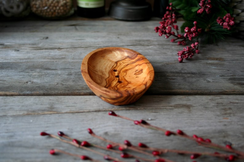 May include: A natural wood soap dish with a light brown color and a grain pattern. The dish has three small holes in the bottom for drainage.