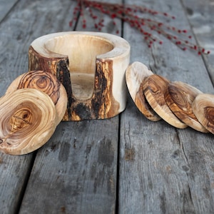Può includere: Set di sei sottobicchieri in legno naturale con un porta bicchieri in legno. I sottobicchieri sono rotondi e hanno un motivo a venature del legno naturale. Il porta bicchieri è realizzato in un pezzo spesso di legno con un foro al centro per un bicchiere.