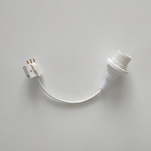 Puede incluir: Un portalámparas blanco con un casquillo roscado, conectado por un cable blanco a un adaptador de enchufe blanco con tres clavijas. Los componentes están dispuestos sobre una superficie blanca.