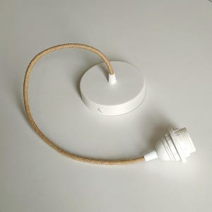 Puede incluir: Una lámpara de techo blanca con un cable cubierto de tela beige. La lámpara incluye una placa de techo redonda y un portalámparas. El cable mide aproximadamente 30 cm de largo.