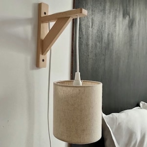 Transparent vägghängande pendellampa med träfäste och enfärgad vit/offwhite/beige lampskärm i linne och bomull