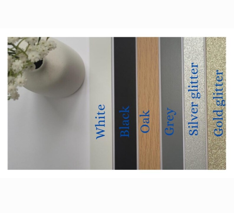 K&ouml;nnte beinhalten: Eine Auswahl an farbigen Bilderrahmenmustern. Die Muster umfassen Wei&szlig;, Schwarz, Eiche, Grau, Silberglitter und Goldglitter. Jedes Muster hat eine Beschriftung mit seinem Farbnamen in blauem Text. Eine wei&szlig;e Vase mit wei&szlig;en Blumen befindet sich in der oberen linken Ecke.